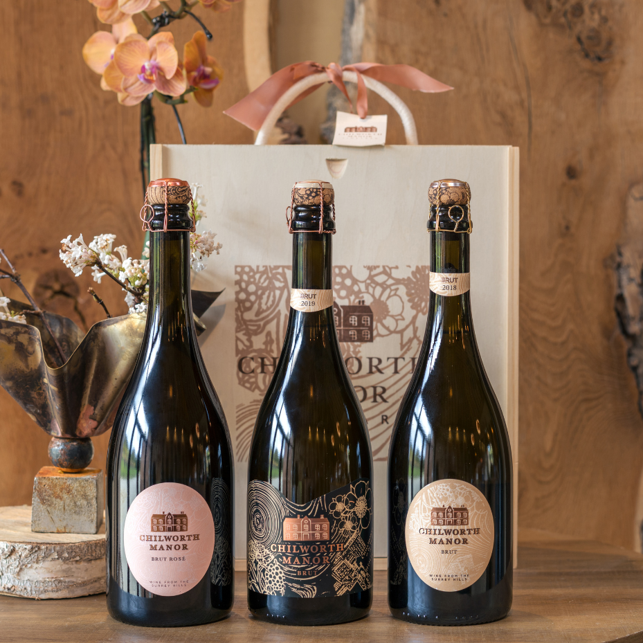 Three bottles of Chilworth Manor wine on a wooden table with a decorative background.