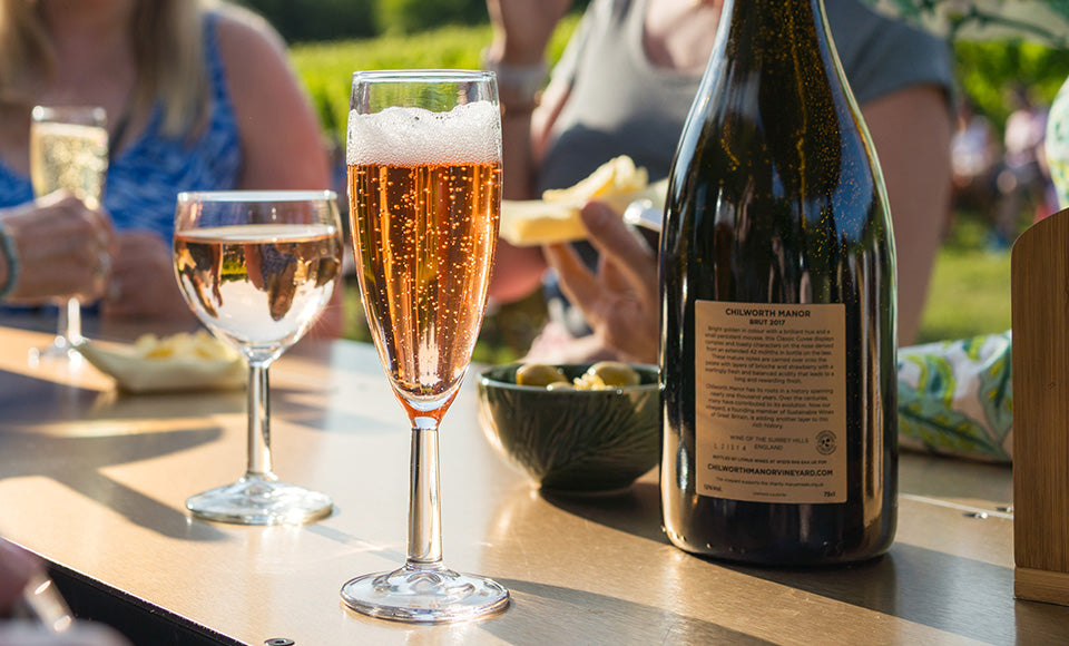 Glasses filled with sparkling white vintage wine, vintage 2025 Still Rose and 2017 Brut Rose from Chilworth Manor Vineyard for the Friday Night Fizz wine tasting experience, paired with appetisers and guests enjoying the hors d'oeuvres in the background