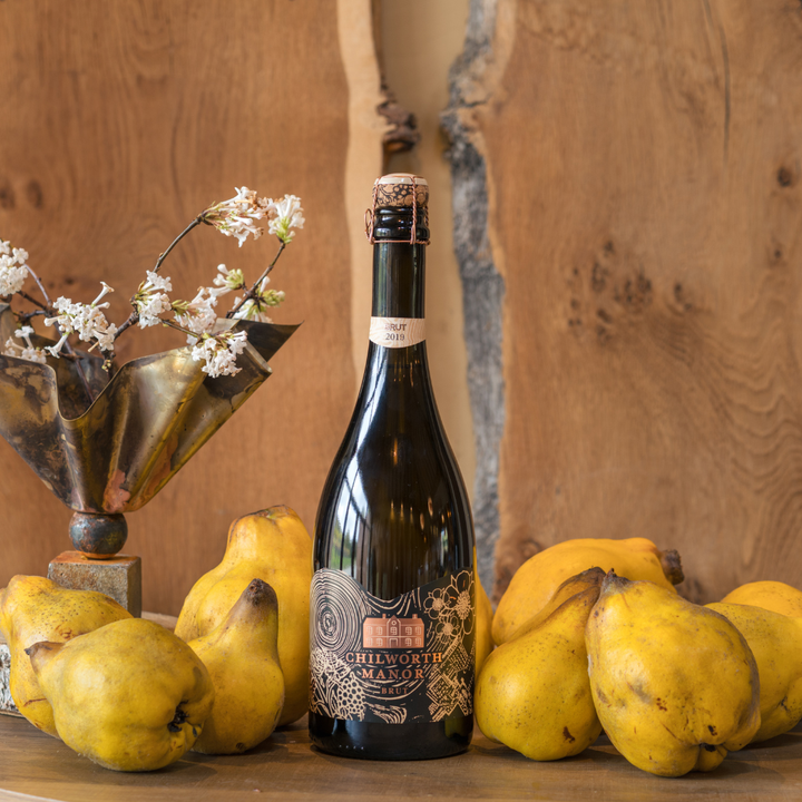 Bottle of Chilworth Manor  Sparkling wine surrounded by quince fruits on a wooden surface.