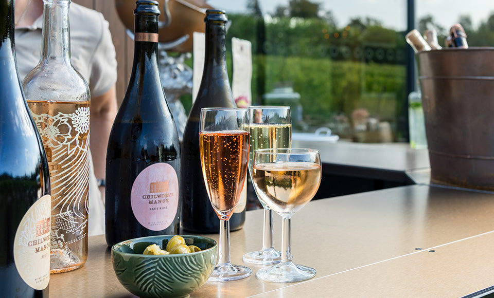 A selection of chilled Chilworth Manor wines, including sparkling white and Brut Rosé, with also still rosé, all served in glasses alongside olive appetisers at the Watch House Tasting Barn bar during an English vineyard tour and tasting event.